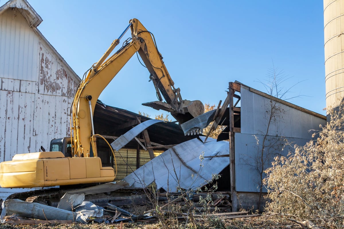 This image shows a close-up view of an excavator in the demolition of an old abandoned barn building.